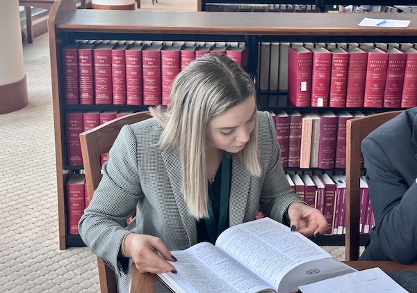 A female student reading a textbook at a table in a courthouse library.