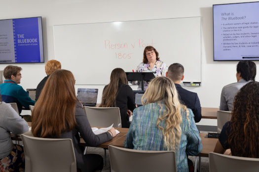 Students at a classroom with teacher standing by the whiteboard.