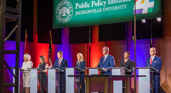a group of 7 professionals behind speaking podiums during a debate