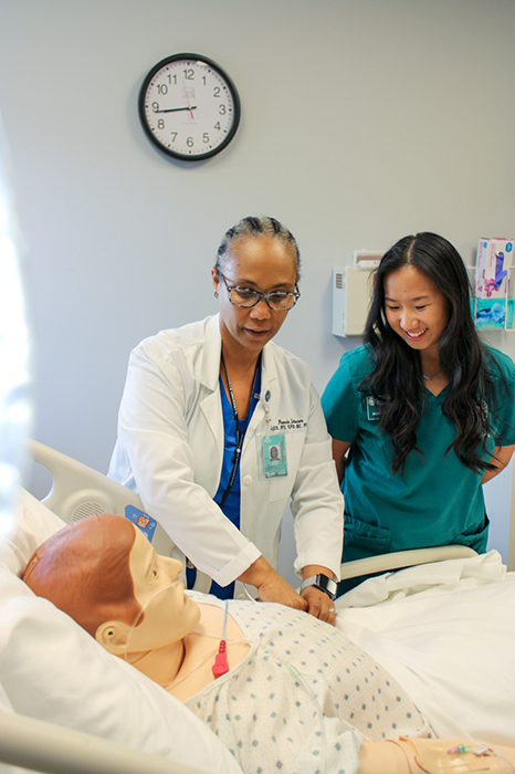A nursing professor teaching a student on a medical maniken.