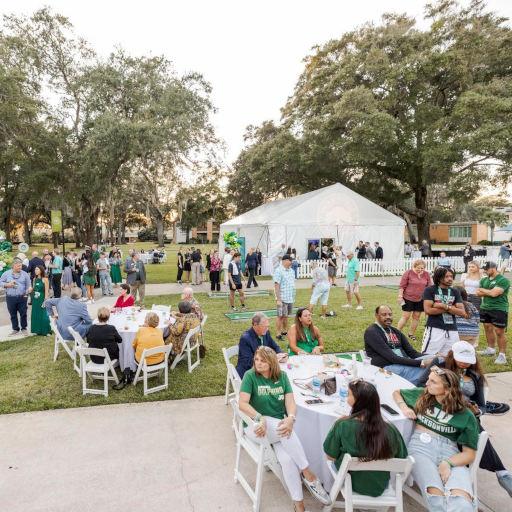a group of people seating at chairs on the picnic on the green lawn at Homecoming
