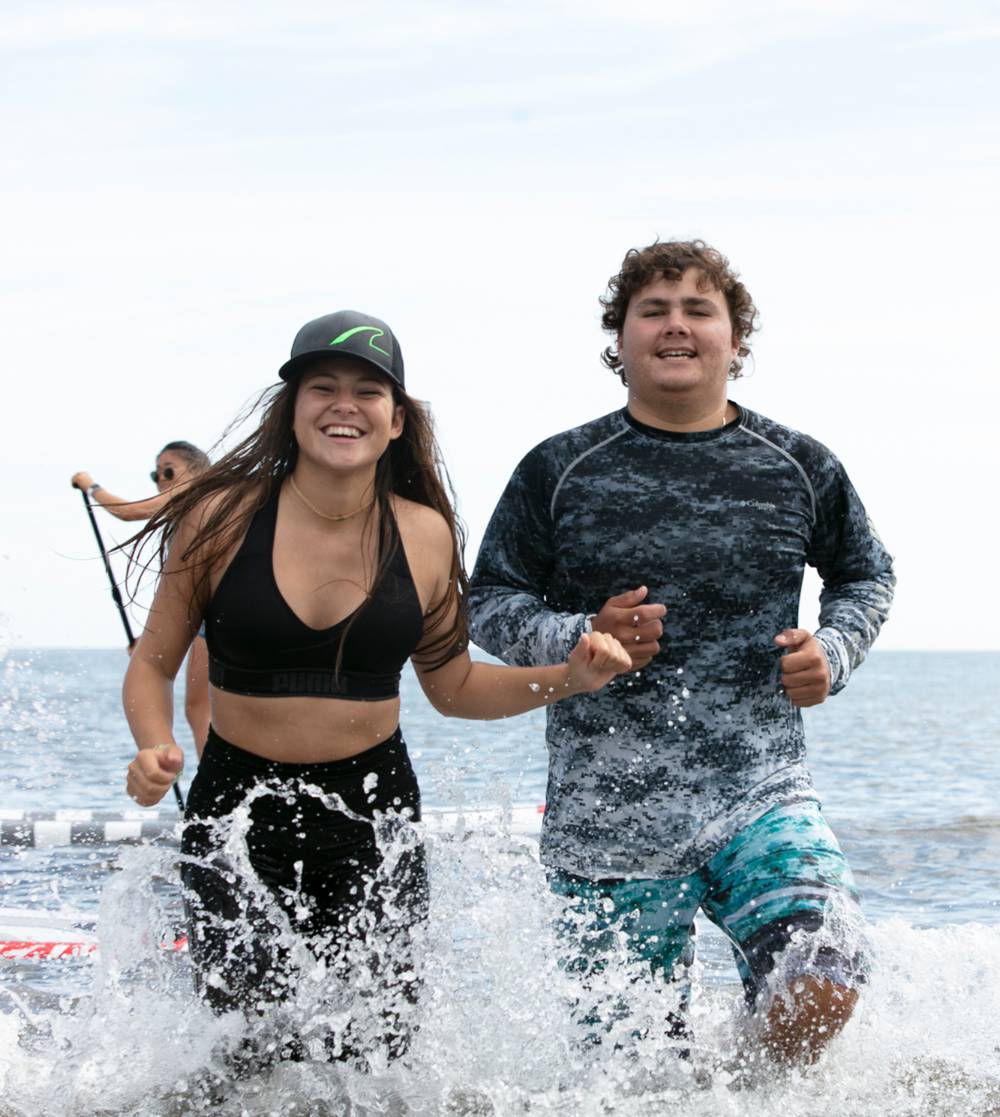 Two JU students at the beach running through the water.