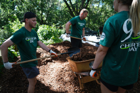 a group of students helping cleaning up leaves, adding mulch and working the campus grounds