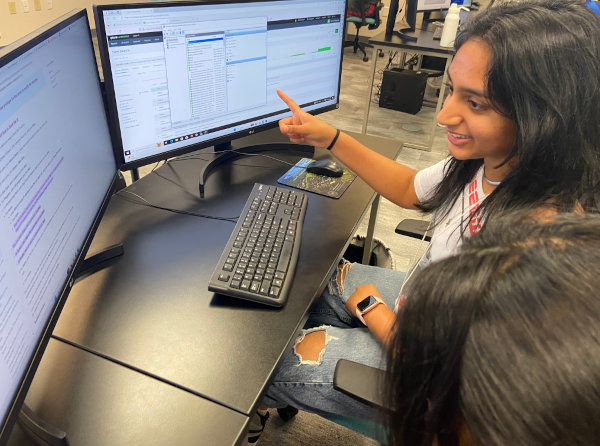 Two students pointing to a laptop in a classroom setting.