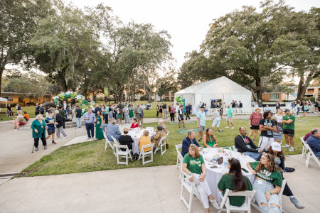 a group of people enjoying a pic nic on a green lawn with white tables and chairs