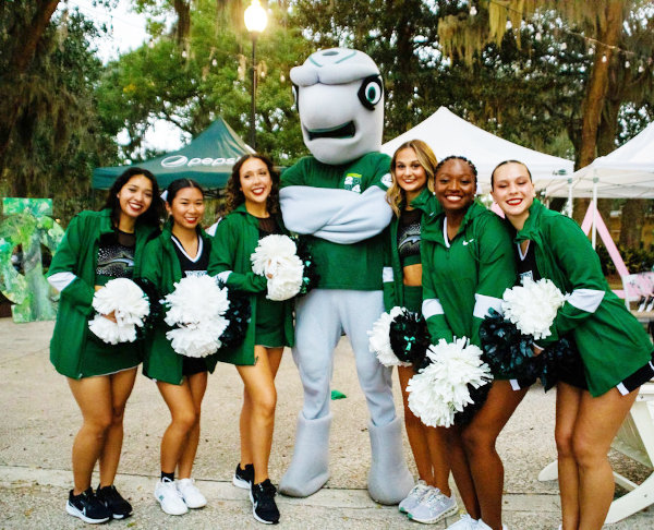 Students cheerleaders wearing JU uniforms posing with Dunk'n JU's mascot
