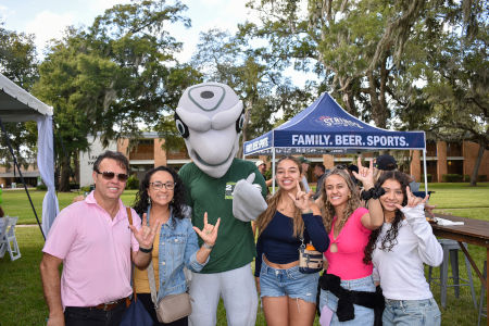 a group of people enjoying a pic nic on a green lawn with white tables and chairs