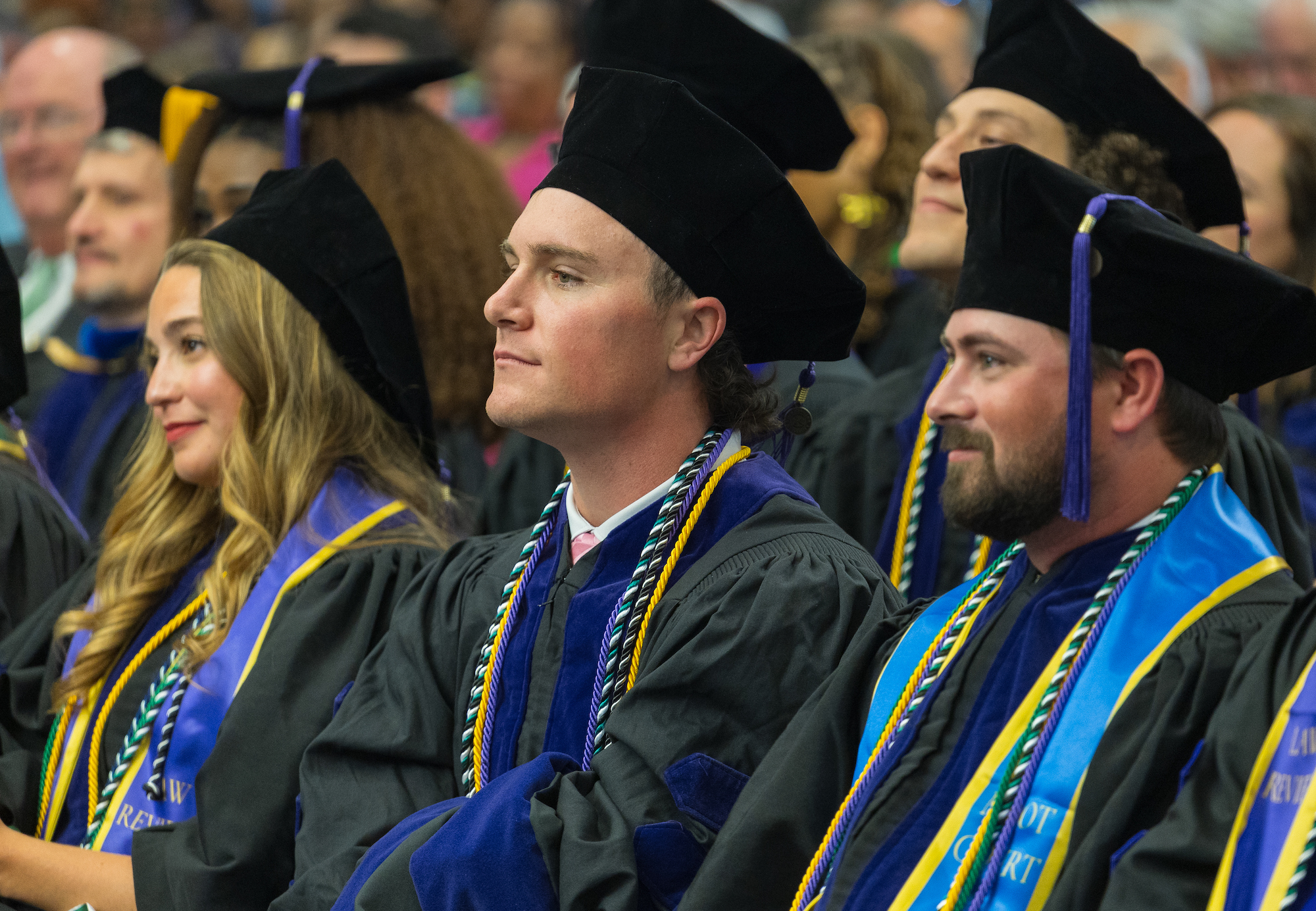 Graduates sitting at graduation in full regalia.