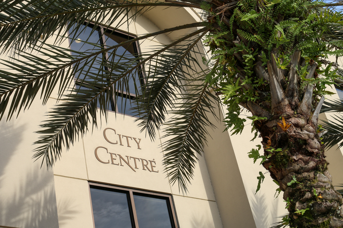 Building face with "City Centre" text behind a palm tree