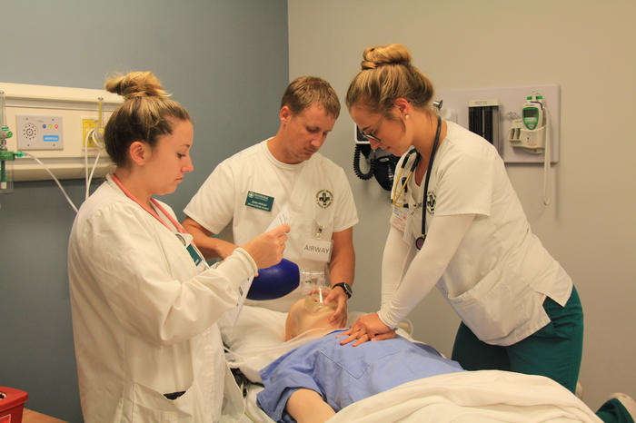 Three nursing students performing various medical procedures on a medical maniken